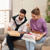 Mann und Frau sitzen auf Couch und packen ihre personalisierten Shopping-Pakete aus