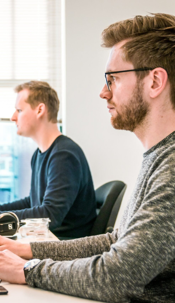 Zwei Männer sitzen an Schreibtischen und arbeiten konzentriert an Computern in einem modernen Büro, zeigt die Effizienz und Flexibilität des Recruitment Outsourcing