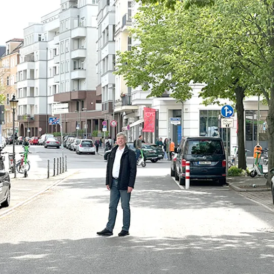 Finanzierungsspezialist Florian Meyer steht auf einer Straße in Berlin Mitte und lächelt in die Kamera. Im Hintergrund sind Eigentumswohnungen zu sehen.