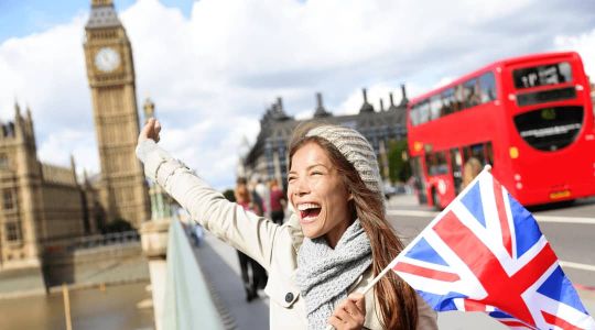 Abitur-Absolventin steht in London vor dem Big Ben mit einer UK-Flagge in der Hand und freut sich über ihr gutes Englisch