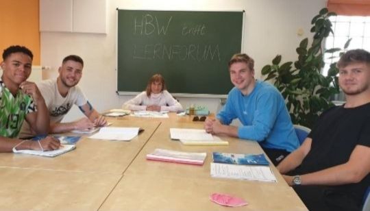 Vier Spieler des HBW sitzen mit ihrer Lehrkraft in einem Klassenzimmer des Lernforums und lächeln in die Kamera