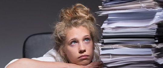 Schülerin der Oberstufe mit großem Stapel von Schulaufgaben neben sich und schaut frustriert in die Luft